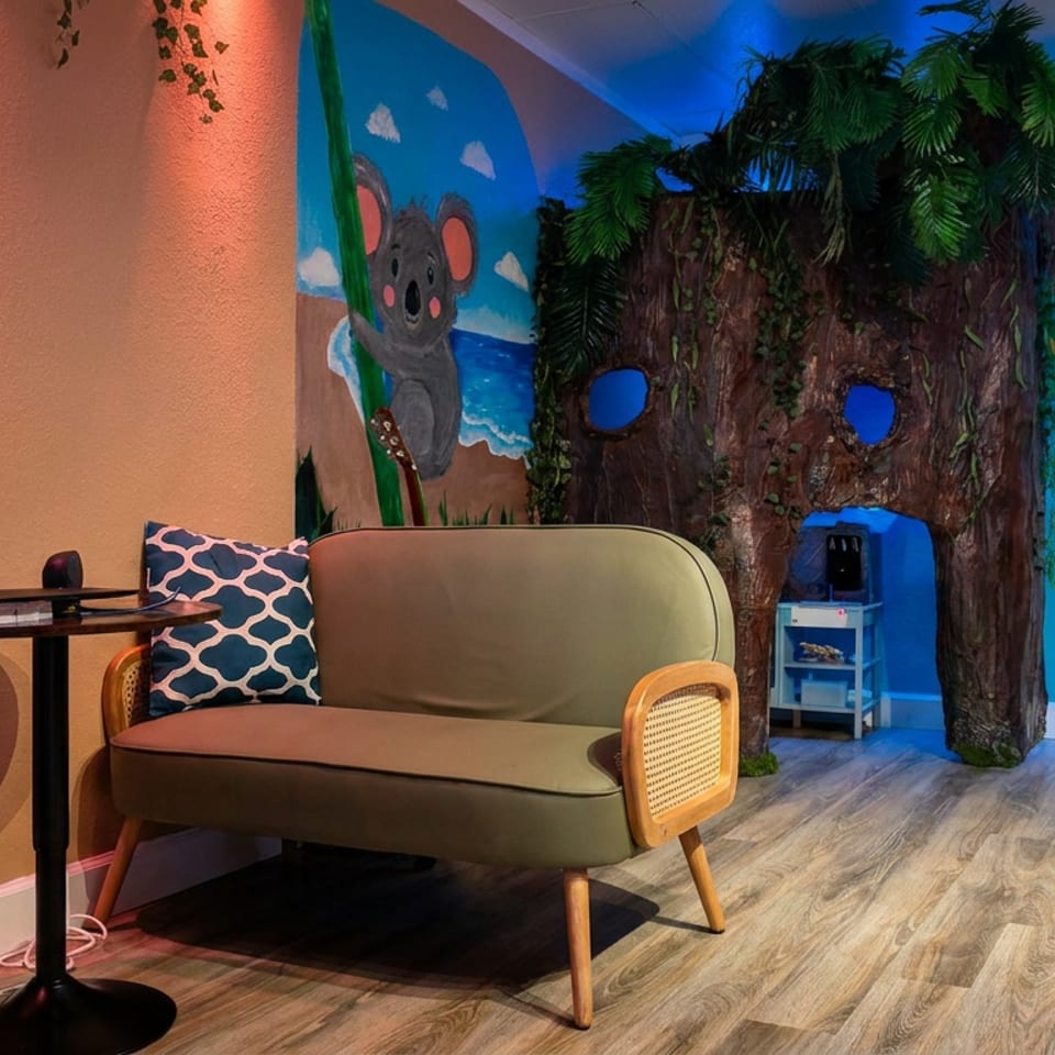 Colorful restaurant lounge with a vintage sofa, tropical tree-themed decor, koala mural, and illuminated liquor display.