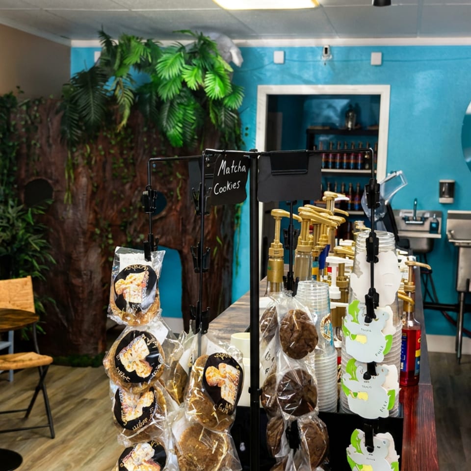 Colorful koala-themed café interior with packaged cookies on display, seating, coffee equipment, and a person beside a refrigerator.