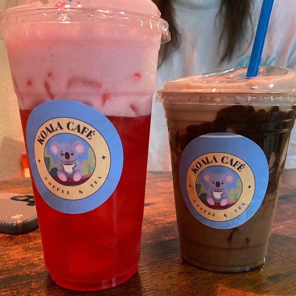 Two Koala Café drinks sit on a wooden table: a pink-and-red iced beverage and a chocolate iced coffee.